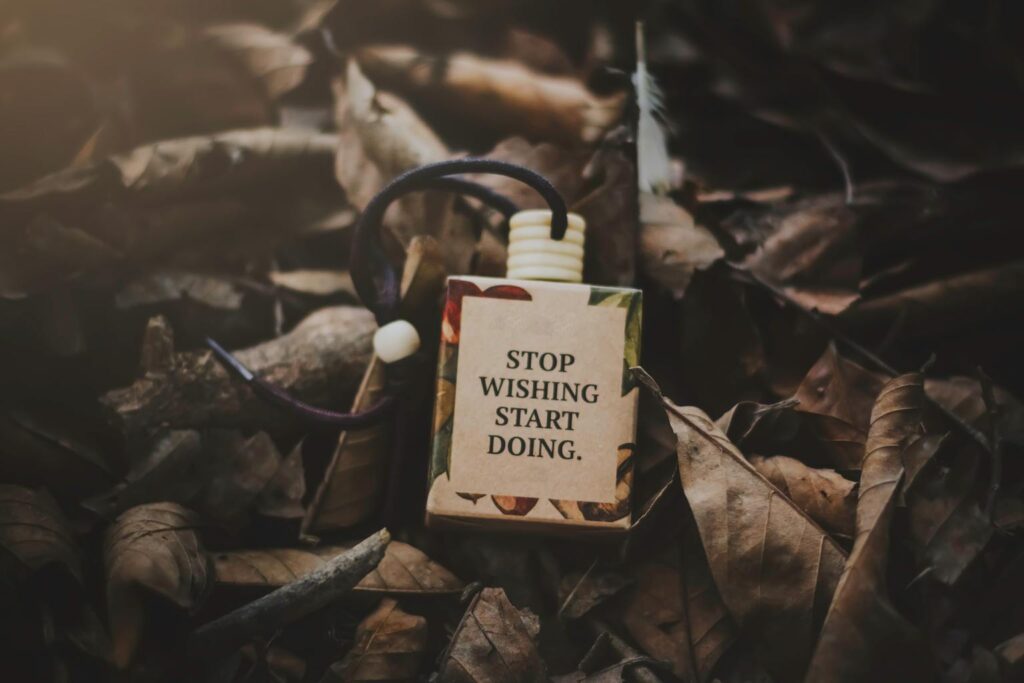 Motivational tag with the words "Stop wishing, start doing" placed on dry leaves.